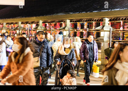 Shogatsu, ins neue Jahr in Nishinomiya Schrein, Japan. Menschen zu Fuß vorbei an Steinlaternen und beleuchtete Boards. Verschwommene Bewegung, auf die junge Mutter konzentrieren. Stockfoto