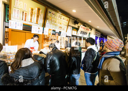 Shogatsu, neues Jahr, Nishisnomiya Schrein, Japan. Menschen kaufen Glücksbringer, des, von Miko, Schrein Dirnen, am Schrein Büro nach Mitternacht. Stockfoto