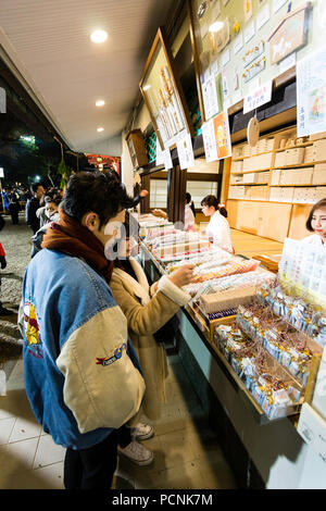 Shogatsu, neues Jahr, Nishisnomiya Schrein, Japan. Paar kaufen Glücksbringer, des, von Miko, Schrein Dirnen, am Schrein Büro nach Mitternacht. Stockfoto