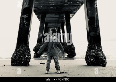 Ein Kleinkind unter einem Steg in der Nähe des Ozeans stehen, der cardwell Jetty, Cardwell, Queensland, Australien Stockfoto