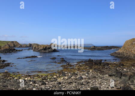 Kleine Inseln und Schären bei Ebbe an exponierten Ballintoy auf der Causeway Coast von Nordirland. Causeway Kopf schwach in der Ferne sichtbar. Stockfoto