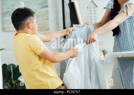 Zugeschnittenes Bild von Mutter und Sohn holding Lappen mit Shirts Stockfoto