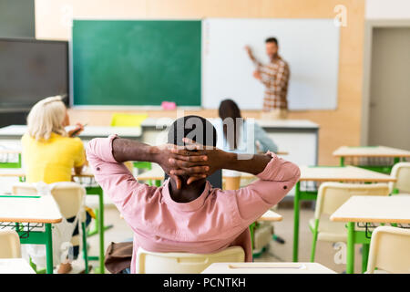 Rückansicht des entspannt afrikanischen amerikanischen Studenten sitzen im Klassenzimmer während der Lektion Stockfoto