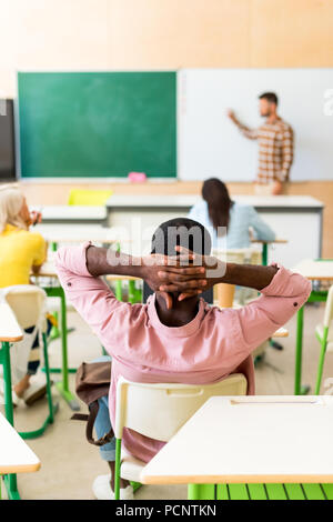 Ansicht der Rückseite des entspannt afrikanischen amerikanischen Studenten sitzen im Klassenzimmer während der Lektion Stockfoto