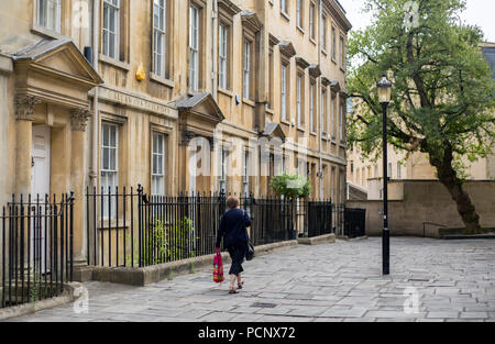 Eine Frau trägt eine rote Einkaufstasche entlang einer Terrasse von georgianischen Stadthäusern in der Badewanne. Stockfoto