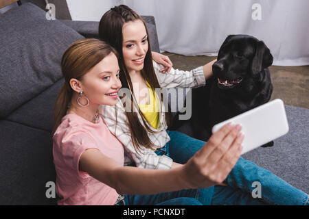 Lächelnde Frau unter selfie mit Freundin und schwarzen Labrador zu Hause Stockfoto