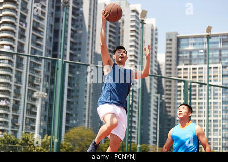 Jungen asiatischen Basketball Spieler gehen, für ein layup während Gegner spielen Verteidigung. Stockfoto