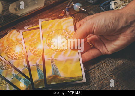 Tarot Karten in der Hand, Pendelwerkzeug und Kristalle auf einem Holzbrett Stockfoto