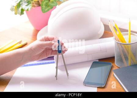 Baupläne in Hand mit Helm, Messen, Mobiltelefon, und Zeichenwerkzeuge Stockfoto