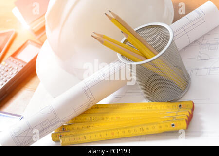 Baupläne mit Helm und Zeichenwerkzeugen auf Blueprints mit Taschenrechner in einem Hintergrund Stockfoto