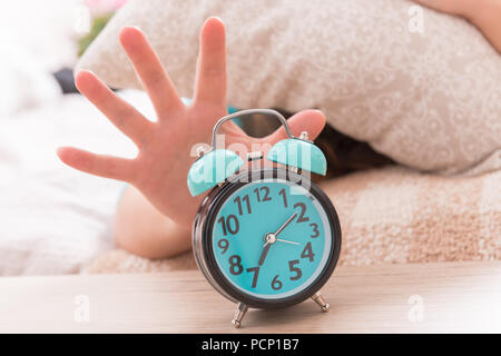 Frau im Bett mit Kissen auf den Kopf und das Erreichen der Wecker, um es auszuschalten Stockfoto