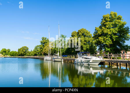 Drei Boote mit einem langen hölzernen Pier oder Promenade entlang Gota Canal in Berg, Schweden. Stockfoto