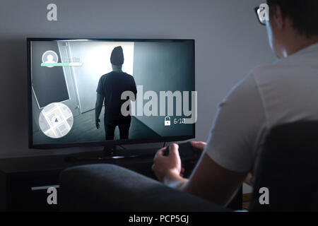 Junge Mann spielt Video Spiel zu Hause mit Konsole. Gamer mit Controller oder Gamepad in der Hand. TV mit Action Spiel auf dem Bildschirm. Spät in der Nacht oder im Dunkeln. Stockfoto