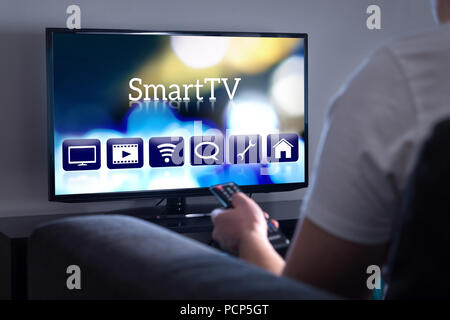 Mann beobachten, Smart-TV. Auswahl Film oder Serie aus dem Menü aus. Person, die Fernbedienung. Benutzeroberfläche auf dem Fernsehbildschirm. Stockfoto