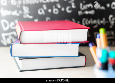 Stack und Stapel Bücher auf dem Tisch vor einer Tafel in der Schule Klassenzimmer. Bildung, Studium, Lehre oder Wissen Konzept. Stockfoto
