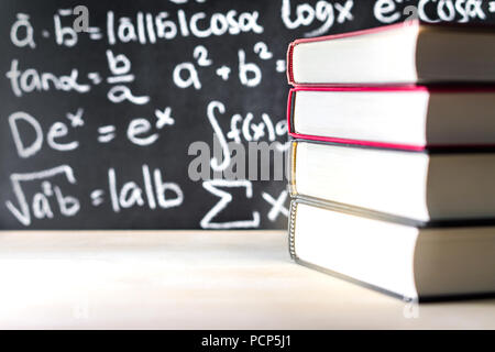 Stack und Stapel Bücher vor einer Tafel in der Schule. Mathematische Gleichung auf die Tafel geschrieben. Stockfoto