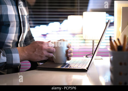 Menschen halten sich an den Händen um Tasse Kaffee oder Tee Becher in home office spät in der Nacht. Krank sein und trinken heißen Getränk oder in Pause bei der Arbeit. Stockfoto