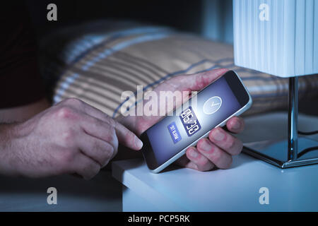 Mann Einstellung Alarm, bevor es in der Nacht zu schlafen. Uhr in Handy. Bis früh Aufwachen am nächsten Morgen zu arbeiten. Stockfoto