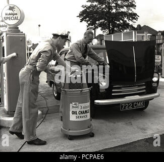 1950, historische,.. beim Service war Serice... auf dem Vorplatz der mobilgas Service Station, zwei unifomed männliche Mitarbeiter kümmern sich um die Kfz des Kunden, wodurch ein Ölwechsel und Motor prüfen, London, England, UK. Stockfoto