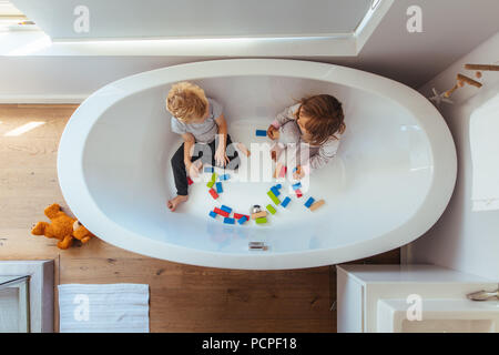 Blick von oben der Geschwister sitzen in der Badewanne mit Holz unterbauen. Kleinen Jungen und Mädchen spielen in einer Badewanne zu Hause. Stockfoto