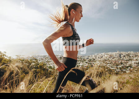 Seitenansicht des String junge Frau in Sportkleidung durch extreme Gelände laufen auf Berg. Läuferin Training für Querfeldein laufen. Stockfoto