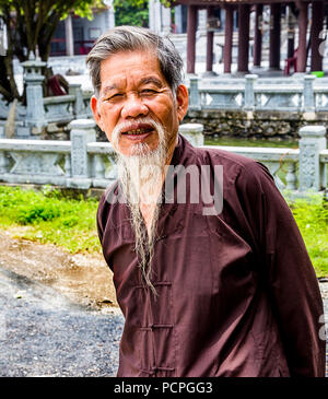 Alte Vietnamesische religiöser Mann mit weißem Bart und Braun asiatischen Mantel jacke Shirt. Stockfoto