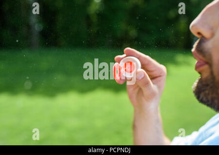 7/8 Schuß von bärtigen Mann bläst Seifenblasen in Park Stockfoto