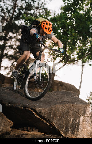 Ansicht von unten auf das extreme Trial Biker reiten auf Felsen im Freien Stockfoto