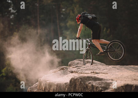 Junge Trial Biker Balancieren auf Vorderrad auf Felsen im Freien Stockfoto