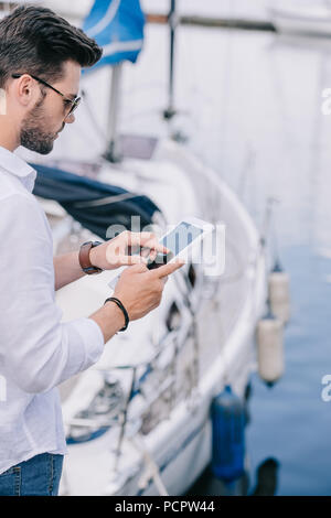 7/8 Schuß des jungen Mannes in Sonnenbrille mit digitalen Tablet bei Yacht Stockfoto