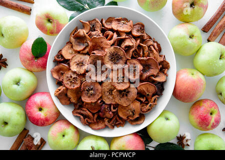 Hausgemachte sonnengetrockneten Bio Apfelscheiben (crispy Apple Chips) mit frischem Apfel und Zimt auf weißem Holz- Hintergrund. Ansicht von oben Stockfoto
