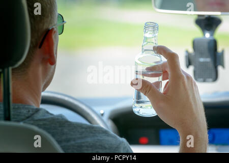 Mann, der ein Auto fährt mit einer Flasche Alkohol. Trinken Sie nicht und Antriebskonzept Stockfoto