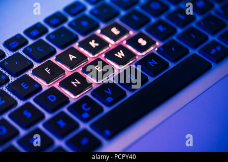 Gefälschte Nachrichten in Rot geschrieben auf einem Laptop Tastatur mit Hintergrundbeleuchtung close-up mit selektiven Fokus in einem blauen Umgebungshelligkeit Stockfoto