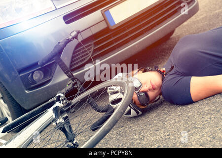 Weibliche Radfahrer liegen auf der Straße nach einem Unfall mit einem Auto und einem Fahrrad Stockfoto