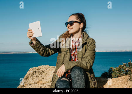 Eine junge schöne Mädchen trifft selfie oder Gespräche mit einem Tablet-PC online oder nimmt Bilder einer schönen Landschaft. Stockfoto