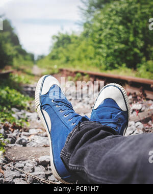 Mann liegt auf einem alten, verlassenen, Gleis, in schwarzen Jeans und blauen canvas Turnschuhe Stockfoto