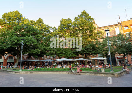 Frankreich, Toulouse - Dezember 9, 2018: eine Frau nächste Fahrrad vor belebte Restaurant Terrassen auf Platz Saint-Georges um Abendessen Zeit zu Het sitzen. Stockfoto