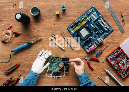 Zugeschnittenes Bild des Menschen mit roboterhand Reparatur Festplatte durch Pinzette Stockfoto