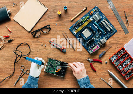 Zugeschnittenes Bild elektronischer Ingenieur mit roboterhand Löten schwer Rive am Tisch Stockfoto