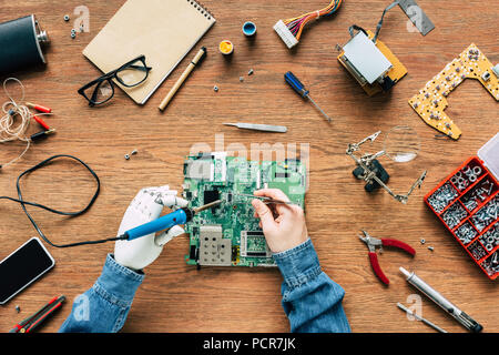 Zugeschnittenes Bild elektronischer Ingenieur mit prothetischen Arm zur Festsetzung motherboard von Lötkolben und Pinzette Stockfoto