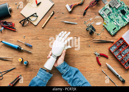 Zugeschnittenes Bild des Menschen mit amputierten setzen auf Roboterhand auf Tabelle mit Tools Stockfoto