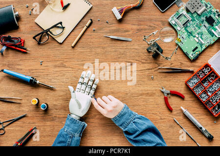 Zugeschnittenes Bild des Menschen zur Festsetzung Roboterhand mit einem Schraubendreher an den hölzernen Tisch Stockfoto