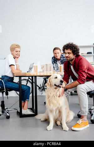 Lächelnden jungen Kollegen an Hund suchen, während im Büro arbeiten Stockfoto