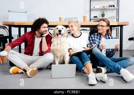 Junge Kollegen mit digitalen Geräten und Hund im Büro Stockfoto