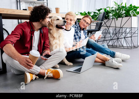 Lächelnden jungen Kollegen an Hund suchen, während zusammen in die Arbeit im Büro Stockfoto