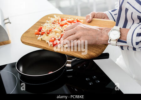 Zugeschnittenes Bild der älteren Frau Gemüse auf die Pfanne in der Küche Stockfoto