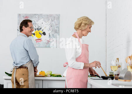 Senior paar Kochen Gemüse auf Pfanne und Schneiden von Gemüse auf Holzbrett in Küche Stockfoto