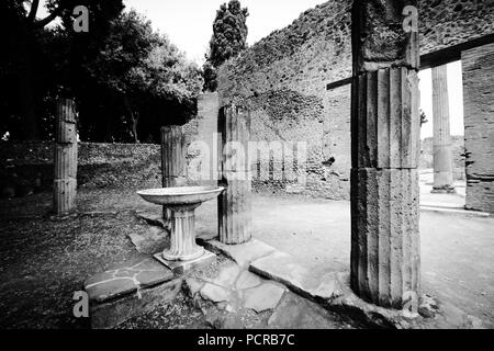 Spalten und ein Vogelbad durch hohe Mauern und Bäume in einem Courtyard in der antiken Stadt Pompeji umgeben, in der Nähe von Neapel, Italien Stockfoto