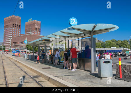 Oslo, Norwegen, 21. Juli 2018: Die Menschen hängen an der Straßenbahnhaltestelle Aker Brygge. Oslo City Hall ist auf dem Hintergrund. Stockfoto