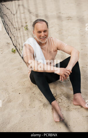 Lächelnd älterer Mann mit Handtuch in der Nähe von Netto auf Sandstrand nach spielen Volleyball Stockfoto